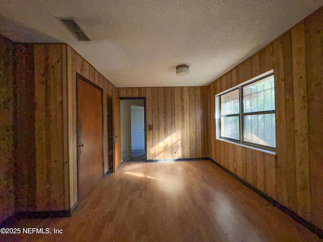 spare room with hardwood / wood-style floors, a textured ceiling, and wood walls