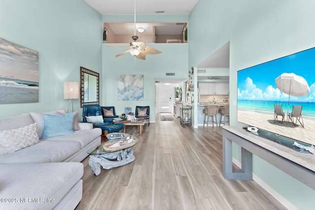 living room featuring a towering ceiling, light hardwood / wood-style flooring, and ceiling fan