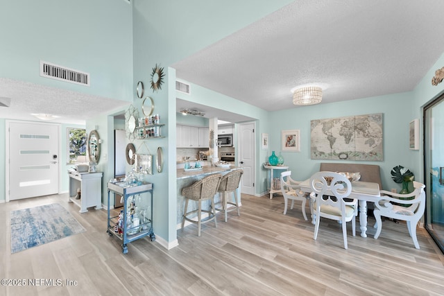 kitchen featuring a breakfast bar area, stainless steel appliances, light hardwood / wood-style floors, a textured ceiling, and white cabinets