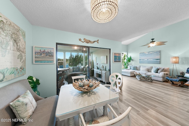 dining room featuring ceiling fan, vaulted ceiling, light hardwood / wood-style flooring, and a textured ceiling