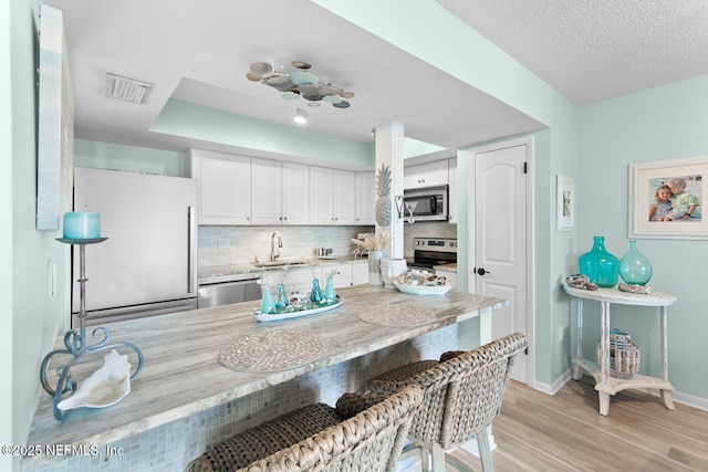 kitchen with white cabinetry, backsplash, light wood-type flooring, and appliances with stainless steel finishes