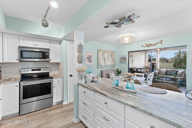 kitchen featuring white cabinetry, stainless steel appliances, light stone counters, tasteful backsplash, and light hardwood / wood-style floors