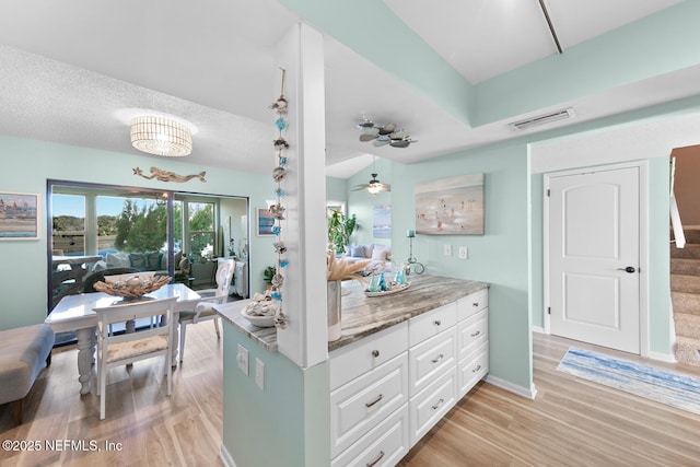 kitchen featuring pendant lighting, white cabinetry, light hardwood / wood-style floors, light stone countertops, and a textured ceiling