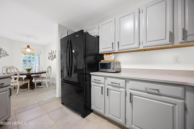 kitchen with hanging light fixtures, black refrigerator, and light tile patterned floors