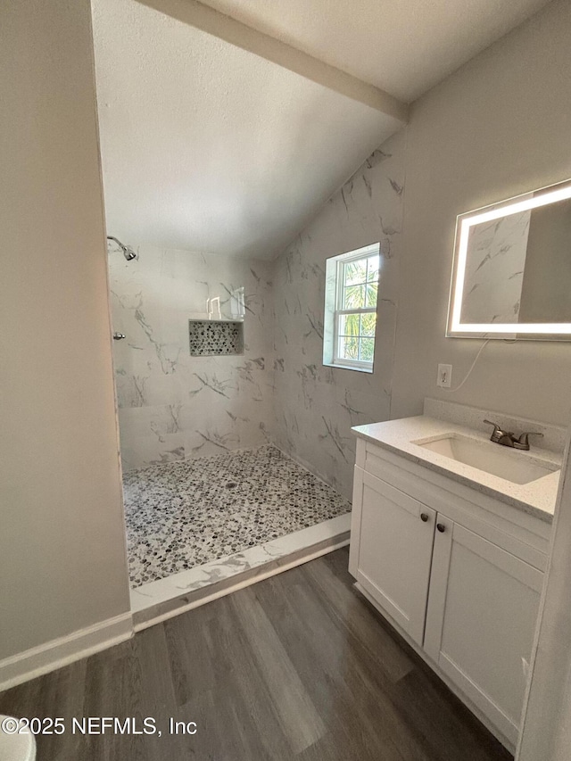 bathroom with hardwood / wood-style floors, tiled shower, vanity, a textured ceiling, and vaulted ceiling