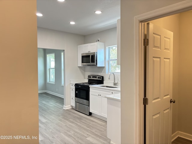 kitchen featuring stainless steel appliances, white cabinetry, sink, and light hardwood / wood-style floors