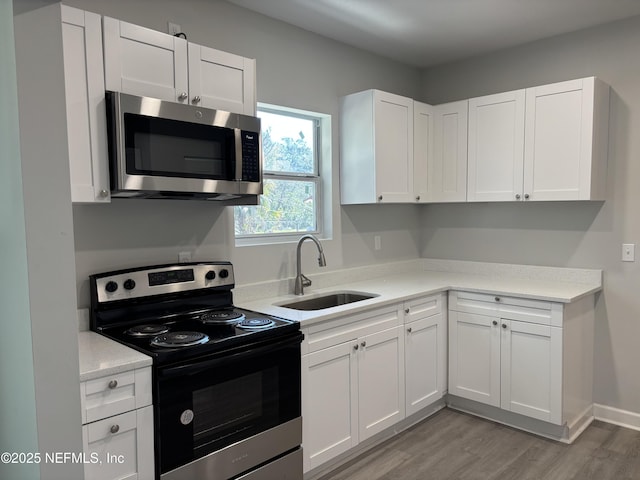 kitchen featuring range with electric stovetop, white cabinetry, sink, and light hardwood / wood-style floors