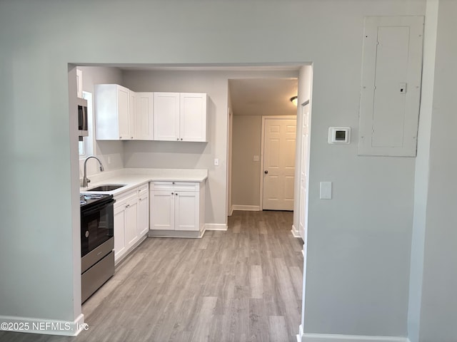 kitchen with sink, white cabinetry, light wood-type flooring, appliances with stainless steel finishes, and electric panel