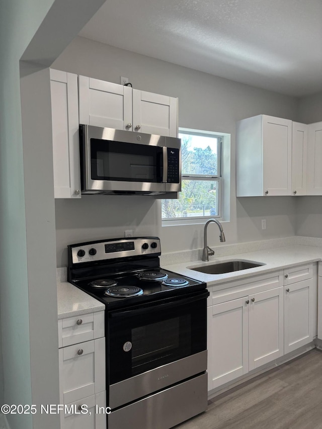 kitchen featuring range with electric stovetop, white cabinetry, sink, and light hardwood / wood-style floors