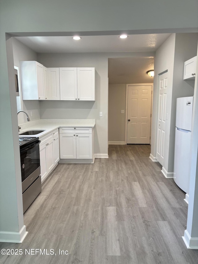 kitchen with sink, light hardwood / wood-style floors, white cabinets, stainless steel electric range oven, and white fridge