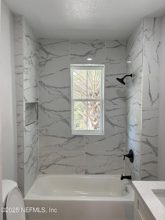 full bathroom featuring vanity, tiled shower / bath combo, and toilet