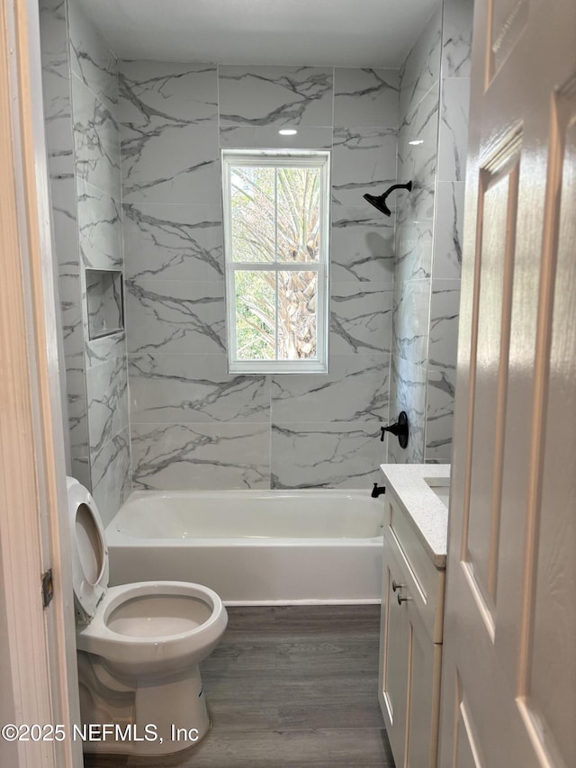 full bathroom featuring vanity, hardwood / wood-style floors, tiled shower / bath combo, and toilet