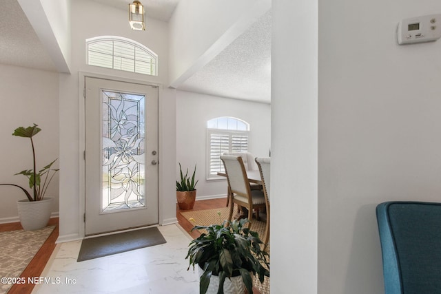 entryway with baseboards, marble finish floor, and a textured ceiling