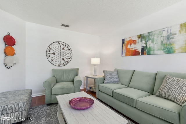 living area featuring visible vents, a textured ceiling, baseboards, and wood finished floors