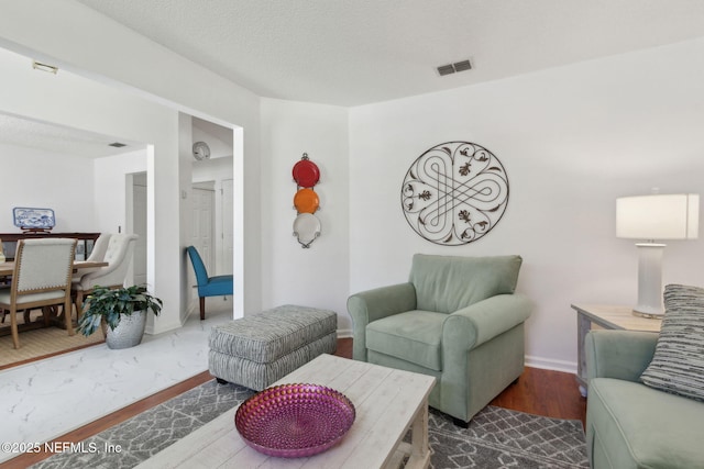 living area with visible vents, baseboards, a textured ceiling, and wood finished floors