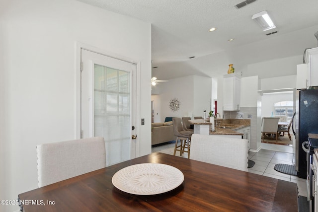 dining area featuring visible vents, a textured ceiling, light tile patterned flooring, lofted ceiling, and ceiling fan