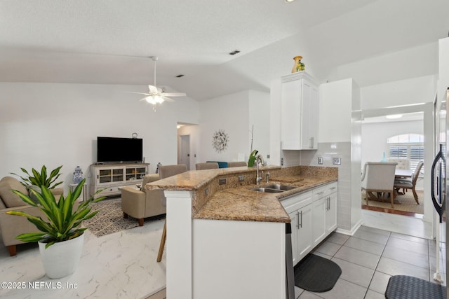 kitchen featuring light stone countertops, lofted ceiling, a peninsula, white cabinetry, and a sink