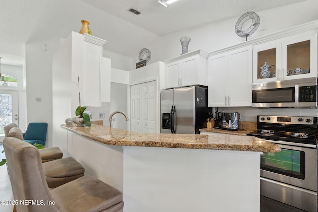 kitchen with light stone counters, decorative backsplash, white cabinets, glass insert cabinets, and appliances with stainless steel finishes