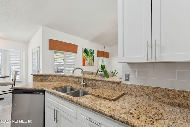 kitchen with light stone counters, decorative backsplash, stainless steel dishwasher, white cabinets, and a sink