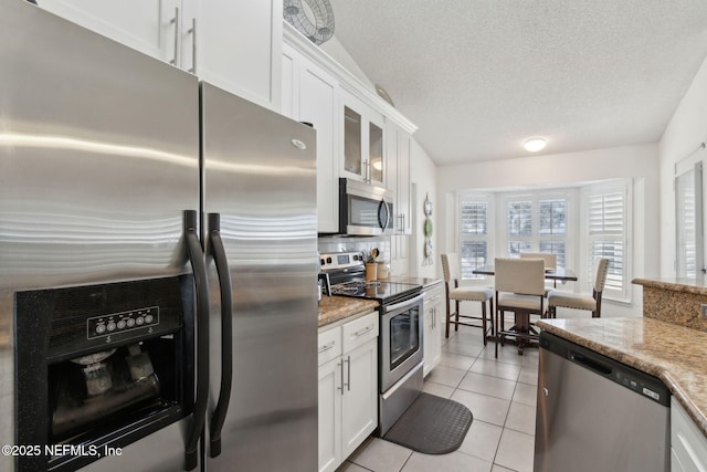 kitchen with light tile patterned floors, appliances with stainless steel finishes, white cabinetry, and a textured ceiling