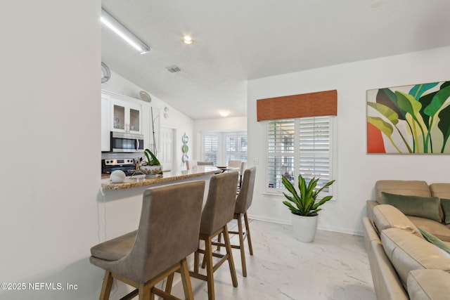 interior space featuring visible vents, stainless steel appliances, white cabinetry, a kitchen breakfast bar, and marble finish floor