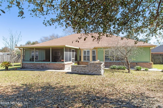 rear view of house featuring fence, roof with shingles, a sunroom, a lawn, and brick siding