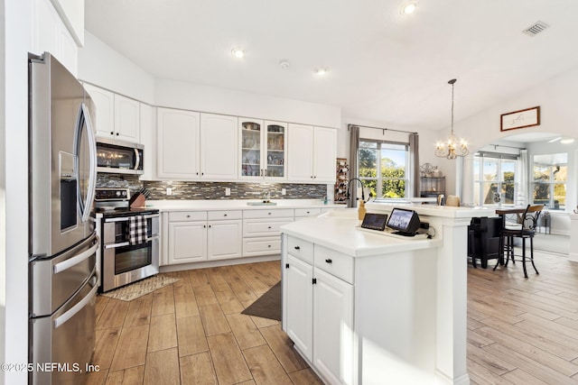 kitchen with sink, white cabinets, hanging light fixtures, a kitchen island with sink, and stainless steel appliances