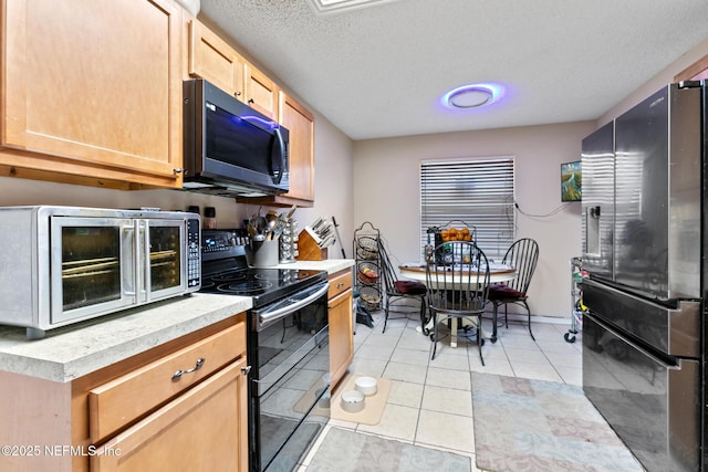 kitchen with light brown cabinets, stainless steel appliances, a textured ceiling, and light tile patterned floors