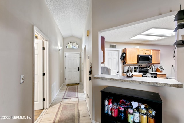 kitchen featuring stainless steel electric stove, lofted ceiling, light tile patterned floors, light brown cabinets, and a textured ceiling