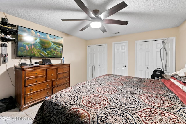 bedroom with multiple closets, light tile patterned flooring, ceiling fan, and a textured ceiling