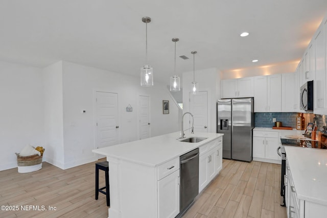 kitchen featuring pendant lighting, sink, stainless steel appliances, an island with sink, and white cabinets