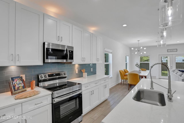 kitchen with sink, backsplash, stainless steel appliances, white cabinets, and decorative light fixtures