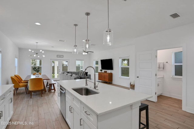 kitchen with sink, light hardwood / wood-style flooring, hanging light fixtures, an island with sink, and white cabinets