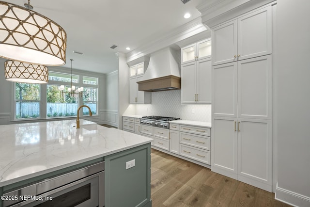 kitchen with appliances with stainless steel finishes, hanging light fixtures, custom exhaust hood, and white cabinets