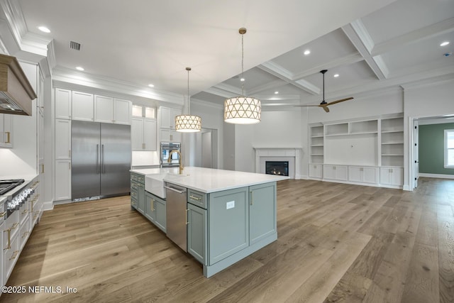 kitchen featuring decorative light fixtures, white cabinetry, coffered ceiling, a kitchen island with sink, and stainless steel appliances