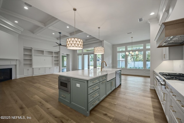 kitchen with coffered ceiling, sink, decorative light fixtures, a center island with sink, and appliances with stainless steel finishes