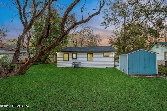 back house at dusk featuring a yard and a storage unit