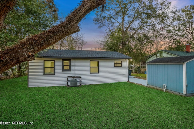 back house at dusk featuring a shed and a lawn