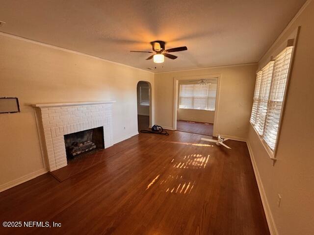 unfurnished living room featuring crown molding, ceiling fan, dark hardwood / wood-style flooring, and a fireplace