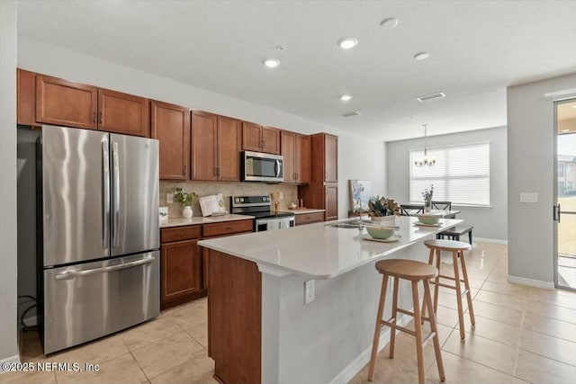 kitchen featuring light tile patterned floors, a kitchen island with sink, hanging light fixtures, stainless steel appliances, and a kitchen bar