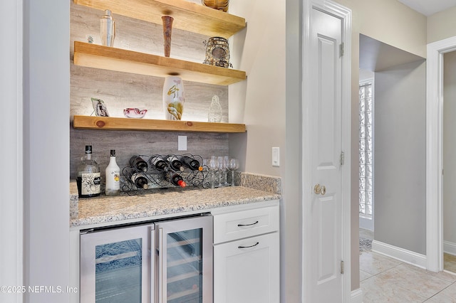 bar featuring white cabinetry, wine cooler, decorative backsplash, light tile patterned floors, and light stone countertops