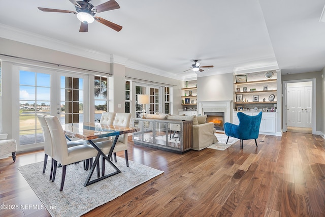 dining room with a tiled fireplace, hardwood / wood-style floors, built in features, and a wealth of natural light