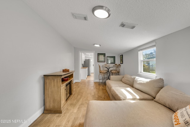 living room with lofted ceiling, a textured ceiling, and light hardwood / wood-style floors