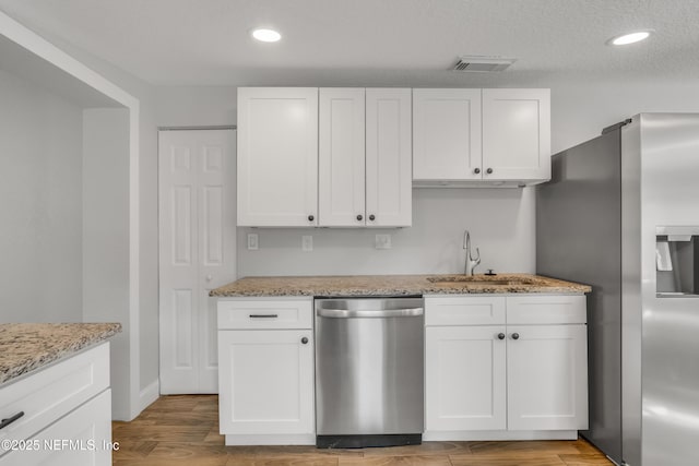 kitchen featuring light stone counters, stainless steel appliances, white cabinets, and light wood-type flooring