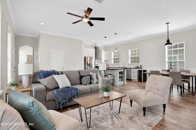 living room featuring wine cooler, crown molding, light hardwood / wood-style floors, and ceiling fan