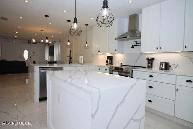 kitchen with pendant lighting, stainless steel appliances, wall chimney exhaust hood, and a kitchen island