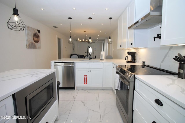 kitchen featuring wall chimney range hood, sink, hanging light fixtures, stainless steel appliances, and white cabinets