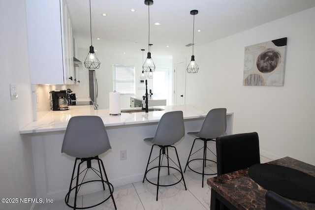 kitchen with sink, a kitchen breakfast bar, kitchen peninsula, pendant lighting, and white cabinets