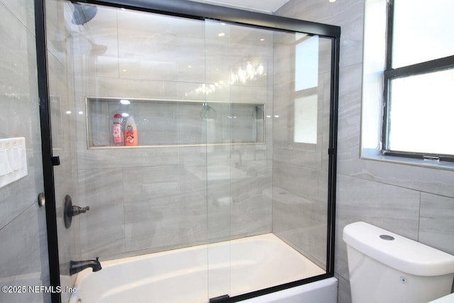 bathroom featuring tile walls, toilet, and combined bath / shower with glass door