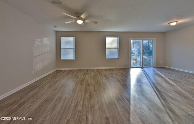 empty room featuring ceiling fan, a textured ceiling, a healthy amount of sunlight, and light wood-type flooring